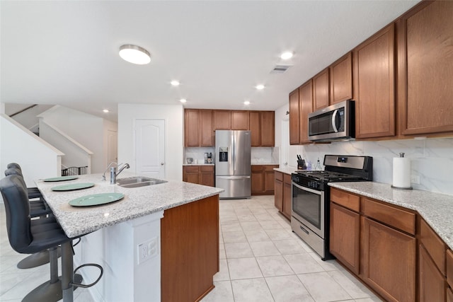 41534 Stampede Stream Dr, Magnolia, TX 77354 - kitchen with visible vents, brown cabinetry, a breakfast bar area, a sink, and appliances with stainless steel finishes