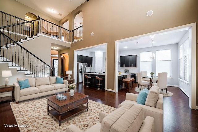 living room featuring stairs, a towering ceiling, baseboards, dark wood-style floors, and arched walkways