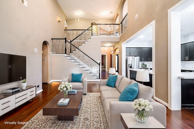 living area featuring arched walkways, dark wood finished floors, a towering ceiling, and stairway