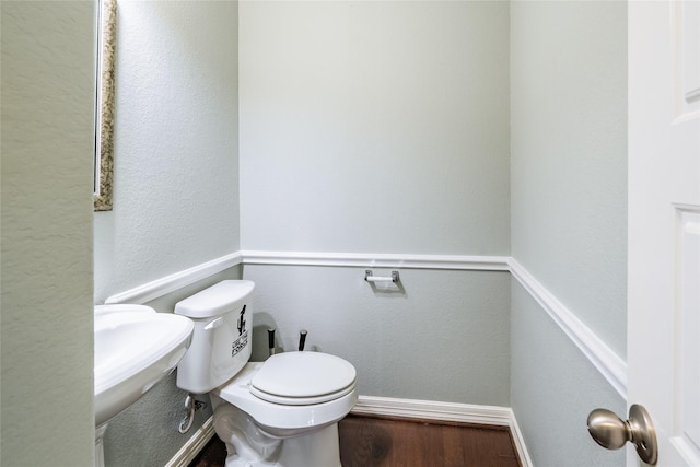 bathroom featuring baseboards, a textured wall, wood finished floors, and toilet