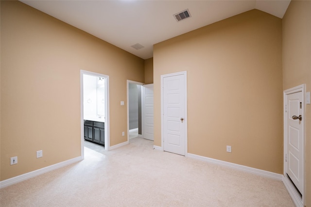 unfurnished bedroom with light colored carpet, visible vents, baseboards, lofted ceiling, and ensuite bathroom