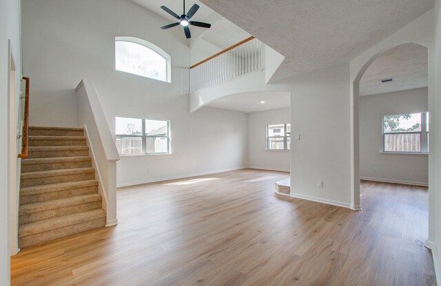 21110 Shelford Ct, Katy, TX 77449 - unfurnished living room featuring arched walkways, ceiling fan, light wood-style flooring, stairway, and high vaulted ceiling
