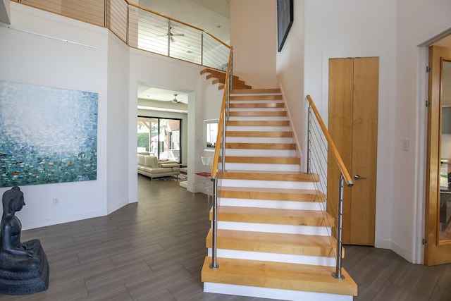 stairs featuring baseboards, a high ceiling, and wood finished floors
