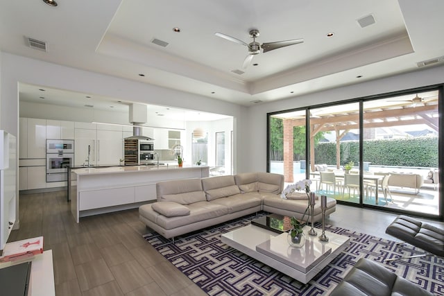living room with a raised ceiling, ceiling fan, and visible vents