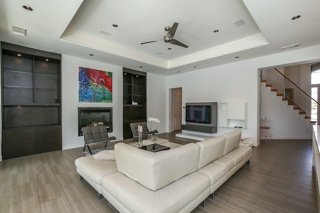 living area featuring a ceiling fan, visible vents, a glass covered fireplace, and a raised ceiling