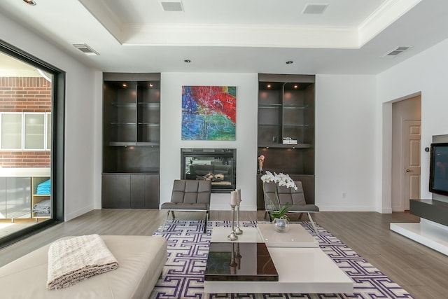 living area featuring ornamental molding, a tray ceiling, wood finished floors, and visible vents