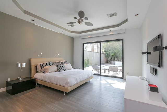 bedroom with access to outside, a tray ceiling, and visible vents
