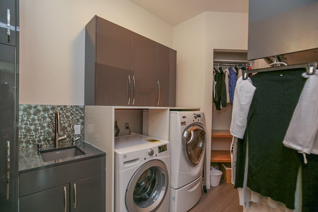clothes washing area with washer and dryer, a sink, light wood finished floors, and cabinet space