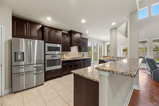 kitchen featuring decorative backsplash, light stone countertops, dark brown cabinets, baseboards, and stainless steel appliances