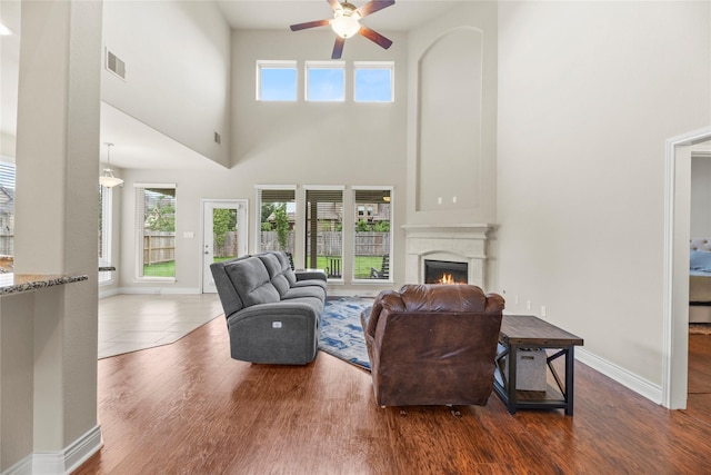 living area featuring visible vents, a healthy amount of sunlight, a high ceiling, a lit fireplace, and a ceiling fan