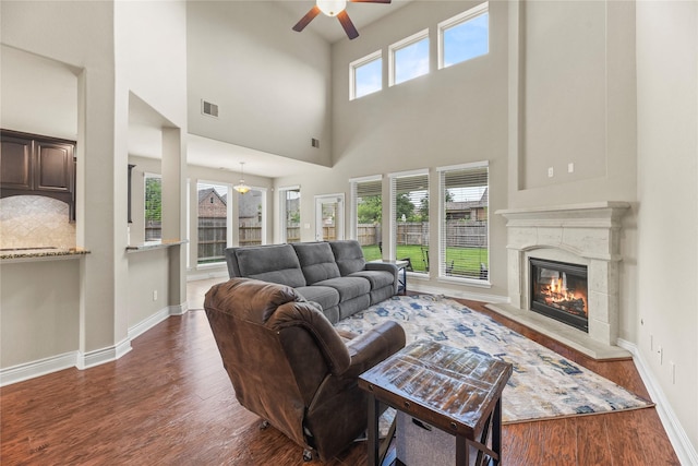living room with a fireplace, a ceiling fan, wood finished floors, a towering ceiling, and visible vents