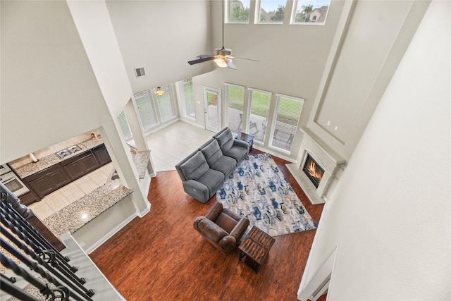 living area featuring ceiling fan, visible vents, wood finished floors, a towering ceiling, and a lit fireplace