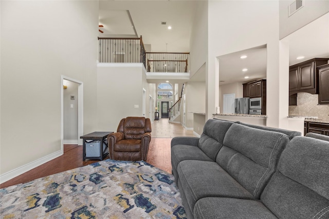 living room featuring a high ceiling, baseboards, wood finished floors, visible vents, and stairway