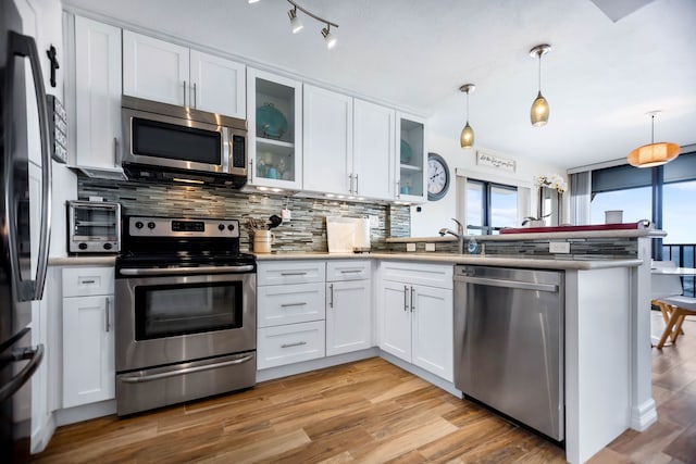 kitchen with a peninsula, a toaster, white cabinets, tasteful backsplash, and stainless steel appliances
