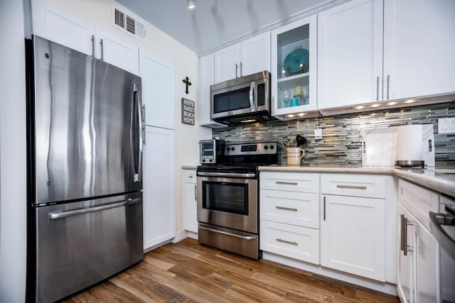 kitchen featuring visible vents, decorative backsplash, glass insert cabinets, white cabinetry, and appliances with stainless steel finishes