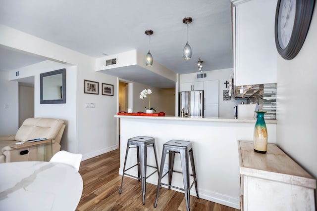 kitchen featuring freestanding refrigerator, a peninsula, baseboards, wood finished floors, and visible vents
