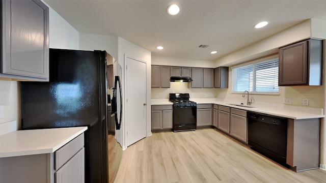 kitchen featuring a sink, light wood-style flooring, under cabinet range hood, visible vents, and black appliances