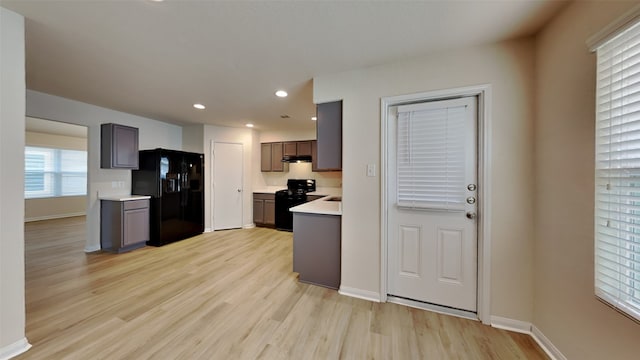 kitchen with light countertops, under cabinet range hood, light wood finished floors, black appliances, and gray cabinetry