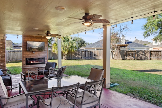 view of patio featuring a glass covered fireplace, a ceiling fan, a fenced backyard, and outdoor dining space