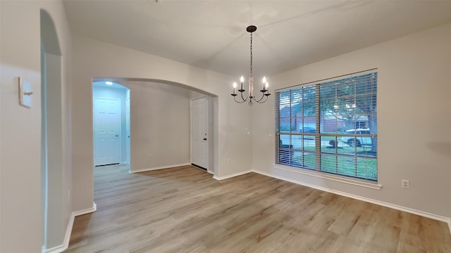 unfurnished dining area featuring arched walkways, baseboards, light wood finished floors, and a chandelier