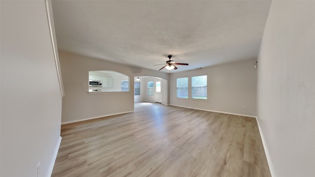 unfurnished room featuring baseboards, arched walkways, ceiling fan, and light wood-type flooring