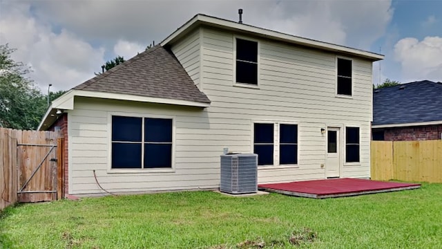 rear view of property featuring fence, a shingled roof, a wooden deck, central AC unit, and a yard