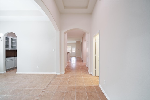hall featuring baseboards, a high ceiling, and light tile patterned floors