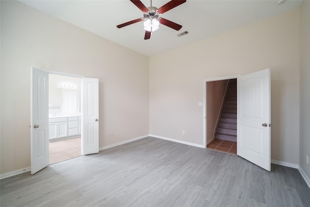 unfurnished bedroom featuring baseboards, ensuite bathroom, light wood finished floors, and visible vents
