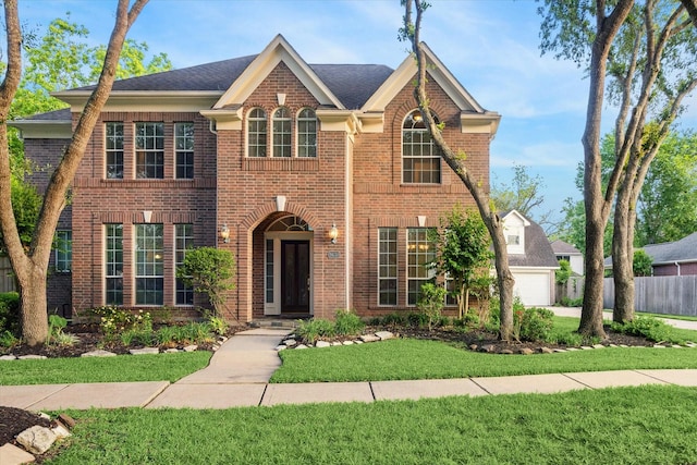 colonial-style house featuring fence, a garage, a front lawn, and brick siding