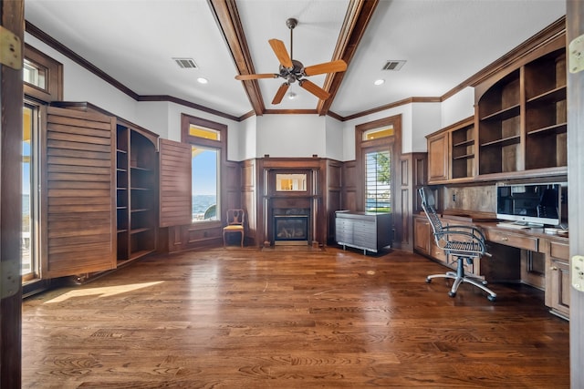 office with visible vents, crown molding, a glass covered fireplace, a ceiling fan, and dark wood finished floors