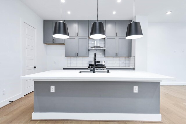 1707 Milby St, Houston, TX 77003 - kitchen with gray cabinets, tasteful backsplash, wall chimney exhaust hood, light countertops, and light wood-style flooring