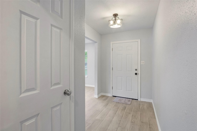 doorway with baseboards, a textured wall, and light wood-style flooring
