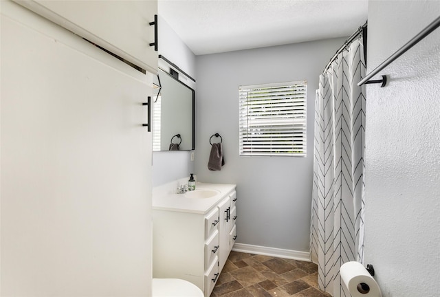 bathroom featuring vanity, toilet, baseboards, stone finish flooring, and curtained shower