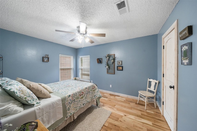 bedroom with ceiling fan, a textured ceiling, visible vents, wood finished floors, and baseboards
