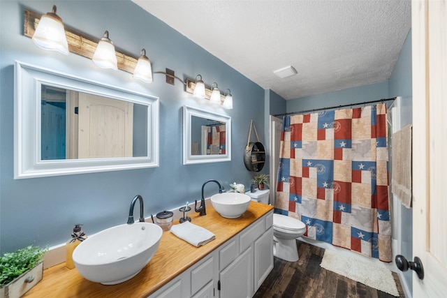 bathroom with a sink, double vanity, toilet, a textured ceiling, and wood finished floors