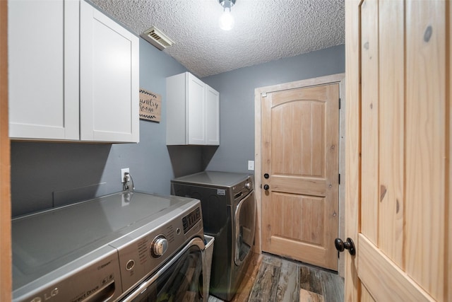 laundry room featuring visible vents, washing machine and dryer, dark wood finished floors, a textured ceiling, and cabinet space