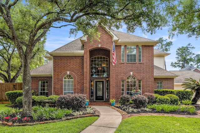 traditional home with brick siding, a shingled roof, fence, and a front yard