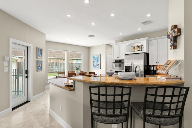 kitchen with light stone countertops, appliances with stainless steel finishes, a kitchen breakfast bar, white cabinetry, and recessed lighting