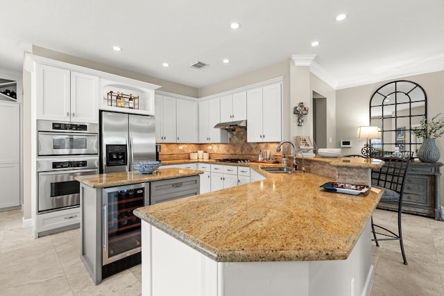 kitchen with wine cooler, a peninsula, light stone countertops, a sink, and appliances with stainless steel finishes