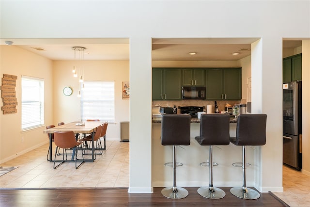 kitchen featuring freestanding refrigerator, black microwave, a breakfast bar area, range, and green cabinets
