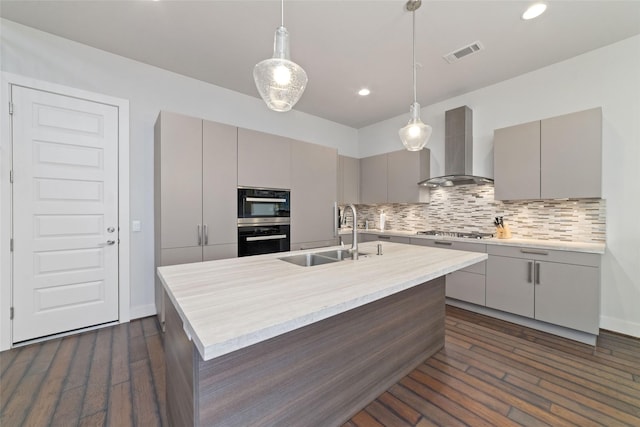 kitchen featuring a sink, gray cabinets, wall chimney exhaust hood, visible vents, and multiple ovens
