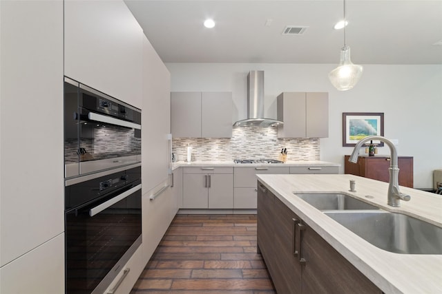 kitchen featuring a sink, light countertops, stainless steel gas cooktop, wall chimney exhaust hood, and visible vents