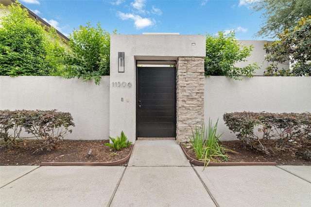 view of exterior entry featuring fence, a gate, and stucco siding