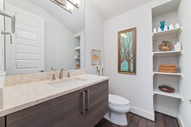bathroom with vaulted ceiling, wood finished floors, baseboards, vanity, and toilet