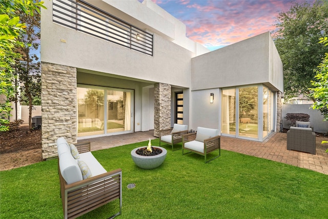 back of property at dusk with a patio, stucco siding, a yard, and stone siding