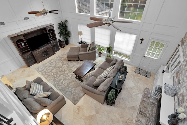 living area with visible vents, a high ceiling, ceiling fan, and a decorative wall