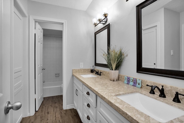 bathroom featuring double vanity, a sink, shower / bathing tub combination, and wood finished floors