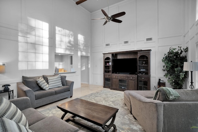 living room with visible vents, a towering ceiling, a decorative wall, and ceiling fan