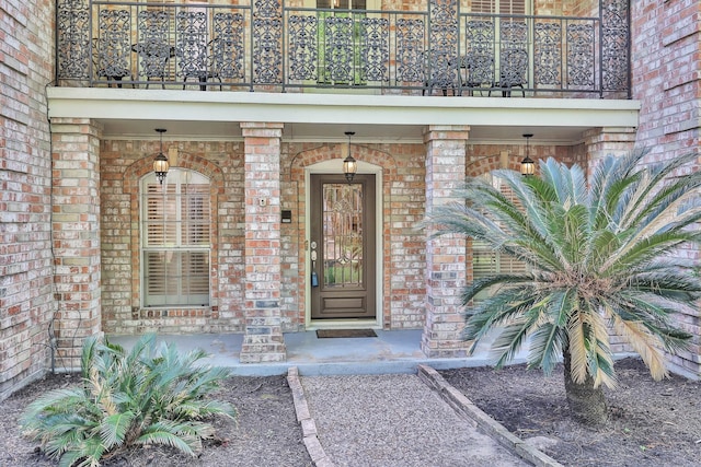 entrance to property with a balcony, covered porch, and brick siding