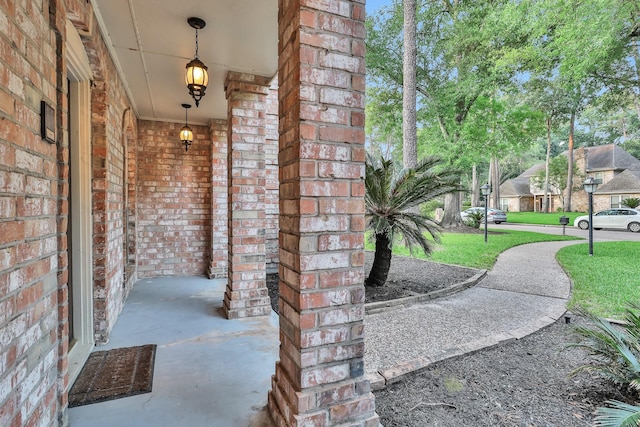 doorway to property featuring covered porch, a yard, and brick siding